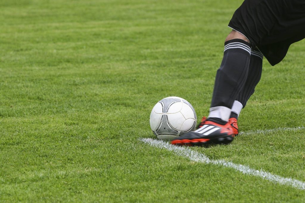 Dynamic shot of a soccer player kicking the ball on a grassy field, showcasing fast-paced sports action.